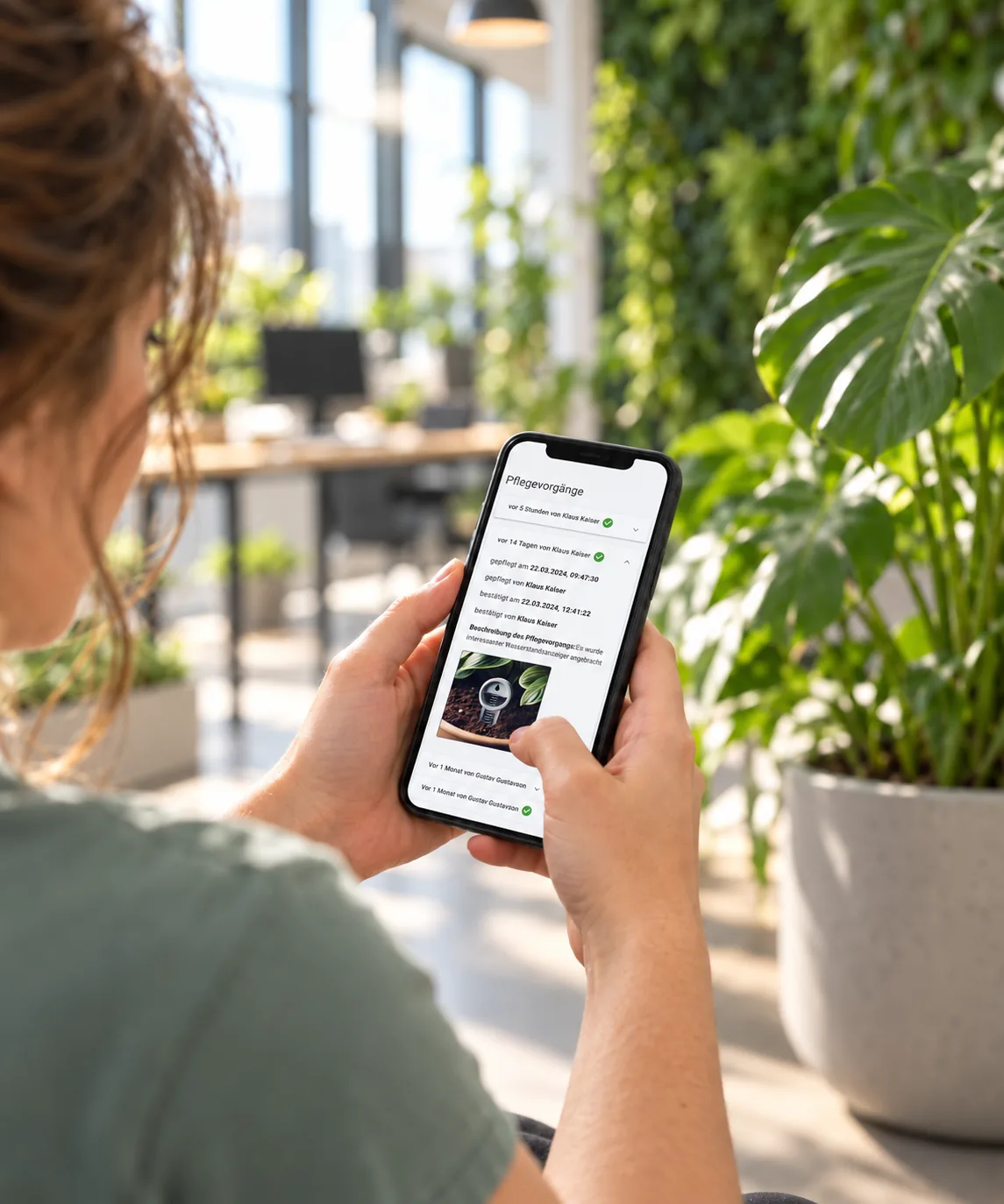 Hände halten ein Smartphone mit der Pflegehistorie in Pflava, im Hintergrund ein begrüntes Büro